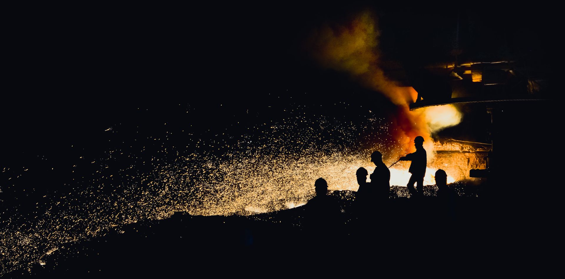 Steelworkers silhouetted against sparks from a furnace tap